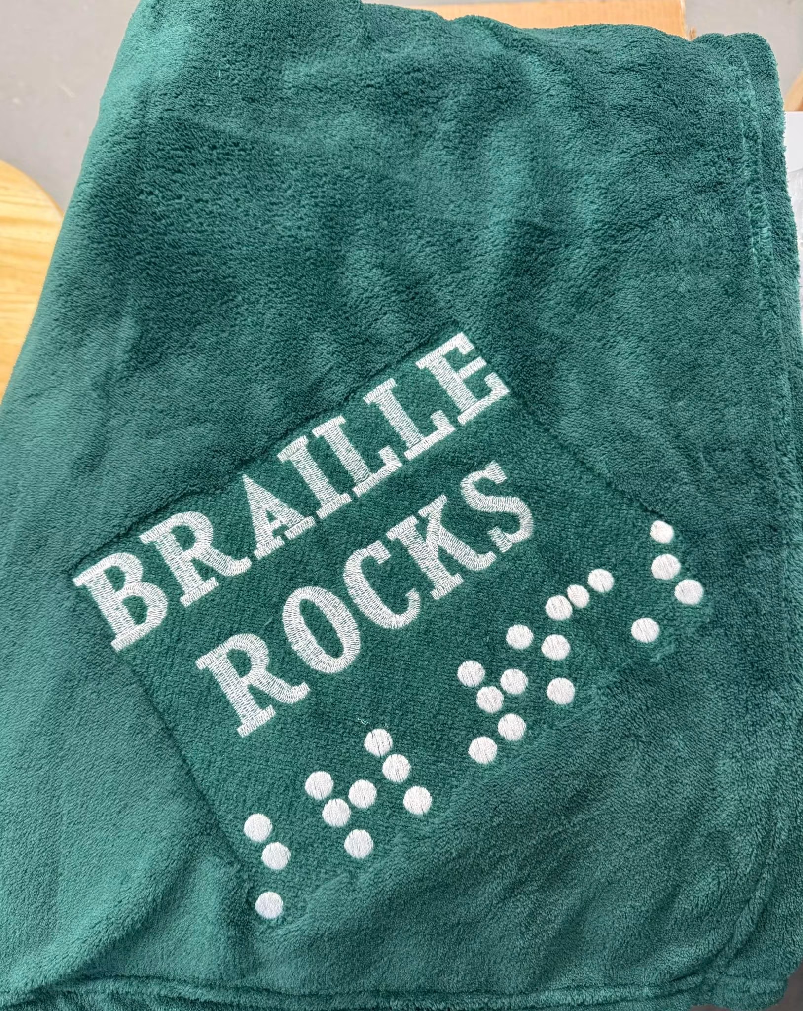 Green blanket with embroidery of Braille Rocks
