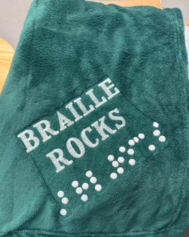 Green blanket with embroidery of Braille Rocks